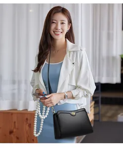 Close-up of minimalist black pebble leather crossbody bag with circular metal logo