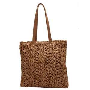 Minimalist hand-woven straw tote bag with brown leather straps for beach holidays