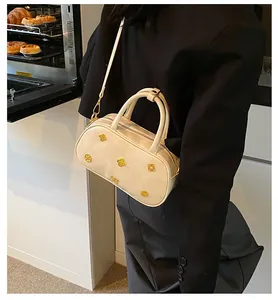 Close-up of cream Boston bag featuring five golden floral accents and detachable strap