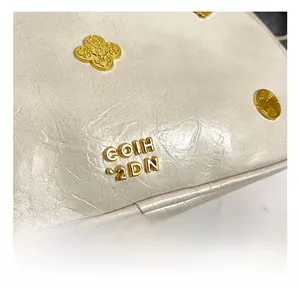 Macro shot of cream embossed leather bag with gold clover logo and metal accents