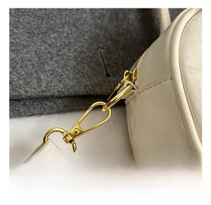 Close-up of golden metal lobster clasp and D-ring on cream leather boston bag