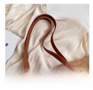 Detail showing high-quality brown leather shoulder strap with contrast stitching on straw tote