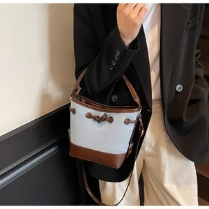 Dettaglio della borsa a secchiello in tela con spalline in pelle marrone su una modella