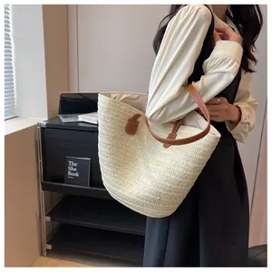 Detail of a large straw tote bag with brown leather handles worn by a model