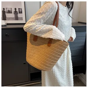 Detail of hand-woven straw tote bag with brown leather handles on a white dress model