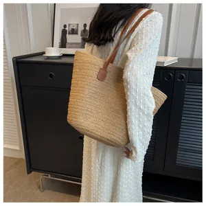 Detail of a large woven straw tote bag with brown leather straps for summer beach use