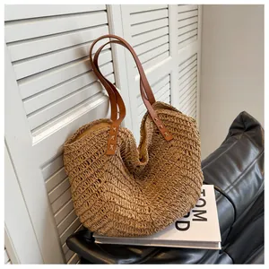 Détail d'un sac cabas en paille tissé avec anses en cuir marron et rivets en métal