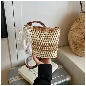 Détail du sac de plage en paille avec nœud en dentelle et breloque en perles