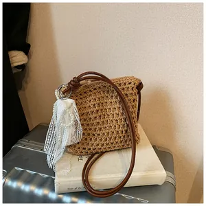 Détail du sac en paille avec breloque perle dentelle et bandoulière en cuir sur des livres
