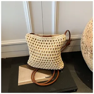 Détail du motif tressé évidé sur sac en paille beige avec bandoulière en cuir marron nouée