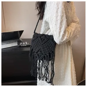 Dettaglio borsa a tracolla nera in macramè con lunghe frange su un abito bianco