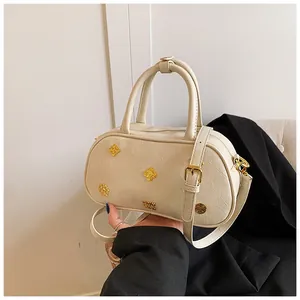 Detail shot of a cream Boston bag featuring vintage gold emblems and textured leather