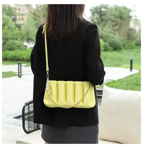 Detail view of yellow pleated handbag with white pearls and gold chain on black blazer
