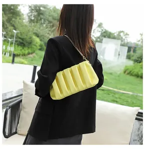 Detail of bright yellow pleated bag featuring a gold chain strap on a black blazer