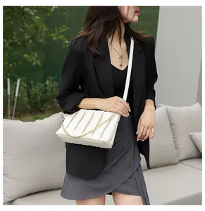 Detail of white pleated handbag featuring vertical accordion folds and gold chain accent
