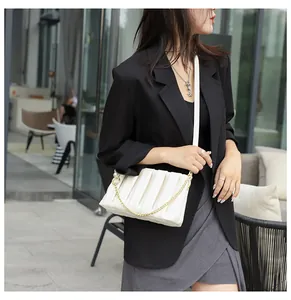 Macro detail of white pleated bag featuring pearl hardware and golden chain strap