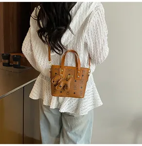 Detail of a brown patterned mini tote bag featuring a cute puppy charm and a shoulder strap