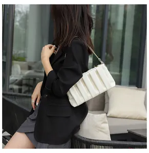 Outdoor lifestyle shot of a white ruched crossbody bag with a golden chain strap