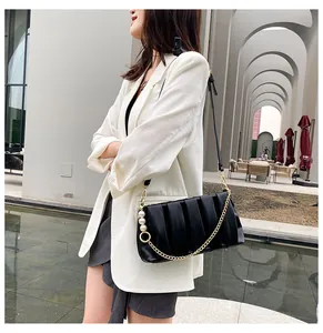 Detail of black pleated shoulder bag with pearl accents and chain on street-style model