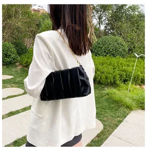Close-up of black ruched square bag with elegant gold chain strap in outdoor setting