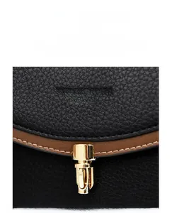 Detail of golden twist lock and textured litchi leather on two-tone crossbody bag