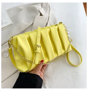 Detail view of bright yellow pleated handbag with gold chain and large pearl charm accessory