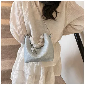 Détail du sac bleu clair à motif crocodile avec anse en perles et bandoulière chaîne