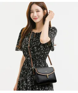 Detail of black pebbled leather crossbody bag with brown strap on a floral dress model