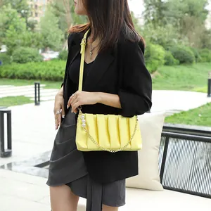 Yellow pleated square bag with pearl chain detail worn by model in casual style