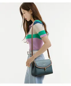 Detail of teal pebble leather crossbody bag with brown trim and gold buckle on a model