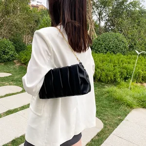 Minimalist black pleated baguette bag with gold chain strap on a white blazer