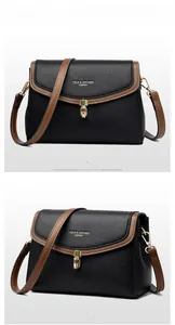 Detail of black lychee leather crossbody bag with brown trim and gold metal clasp