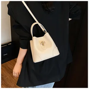 Crossbody carry of a cream-colored bucket bag with lychee texture and golden clasp