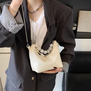 Sac croissant crème chic avec gaufrage croco, poignée en perles et chaîne sur le mannequin