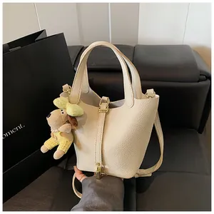 Detail of beige lychee leather bucket bag with gold lock and cute puppy charm accessory