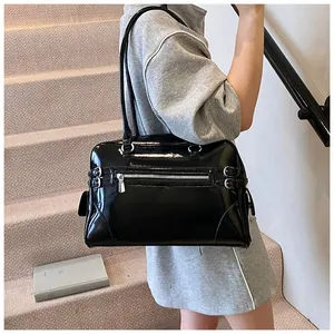 Detail of black patent leather tote bag featuring silver zippers and stylish buckle straps