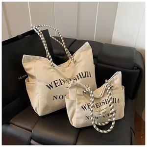 Détail de sacs cabas en toile de deux tailles avec imprimé lettres et poignées en tweed