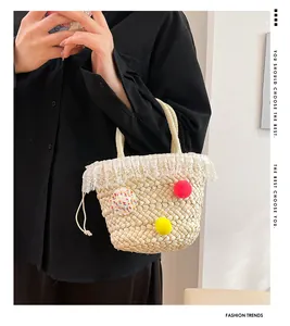 Detail van handgemaakte strooien tas met witte kant, kleurrijke pompons en handgrepen