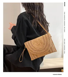 Detail of woven straw envelope clutch with scalloped texture and detachable strap worn by model