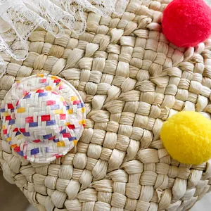 Detail van strooien tas met witte kant, kleurrijke pompons en een mini gestreepte hoed hanger