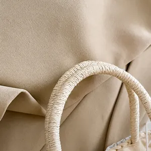 Detail van geweven strohandvat op beige draagtas, focus op textuur en zachte handgreep