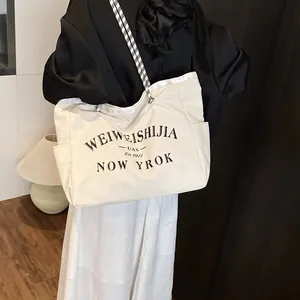Grand sac cabas en toile avec imprimé lettres et bandoulière à damier porté par un mannequin