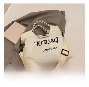 Detail of off-white fabric tote bag featuring WWSJ logo and woven handle on gray blazer