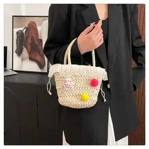 Detail van strooien handtas met witte kanten rand, kleurrijke pompons en trekkoordsluiting