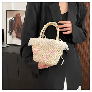 Detail van handgemaakte strooien handtas met witte kantafwerking en roze strikken van lint