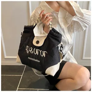 Close-up of black and white canvas tote bag with woven handles and letter embroidery