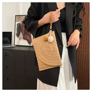 Detailed straw woven envelope clutch featuring decorative fluffy pom poms and wrist strap