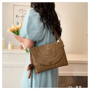 Detail of straw woven envelope bag featuring dual-tone pompom charms and leather strap