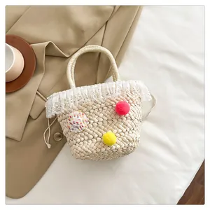 Detail van gevlochten strohandtas met roze pompon en witte kanten afwerking