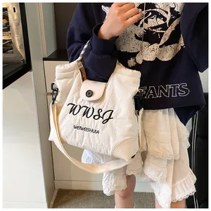 Detail of off-white canvas tote bag featuring black letter embroidery and button closure